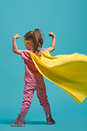 Selbstbewusstes Kind mit gelben Cape nimmt starke Power Pose ein.
